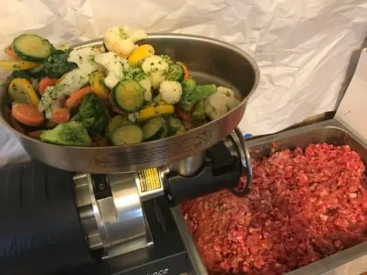 this image shows raw dog food being made at home. it has raw chicken and vegetables 